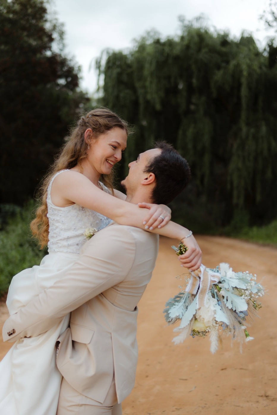 Anrie and Dirk: groom lifting his bride on a tree-lined dirt road